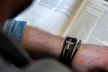 Um homem segura um livro e usa uma pulseira com uma cruz.