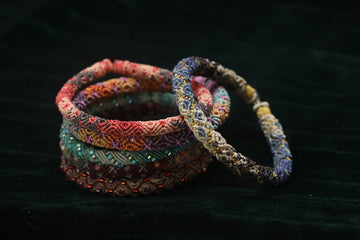 Conjunto de pulseiras de miçangas coloridas sobre tecido escuro.